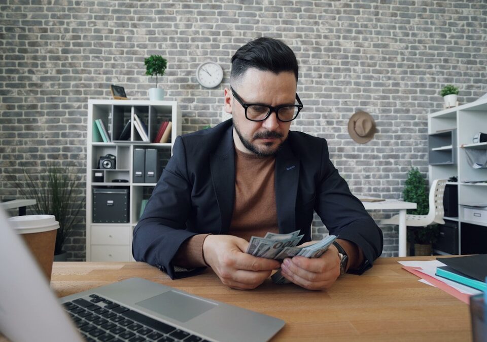 Empreendedorismo e Finanças: Dicas para Cuidar Bem do Seu Dinheiro a man sitting at a table with a laptop and money