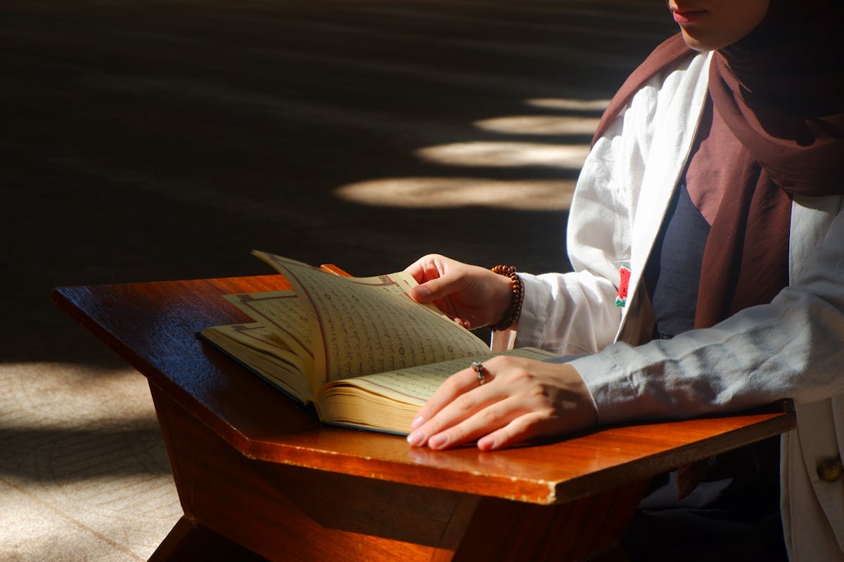 Woman Reading Quran in Sunlit Mosque Interior