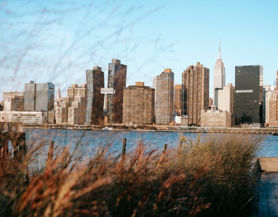 Quanto custa viajar para os EUA? Calm Hudson River flowing near modern district with high rise buildings placed in New York under cloudless blue sky in daytime