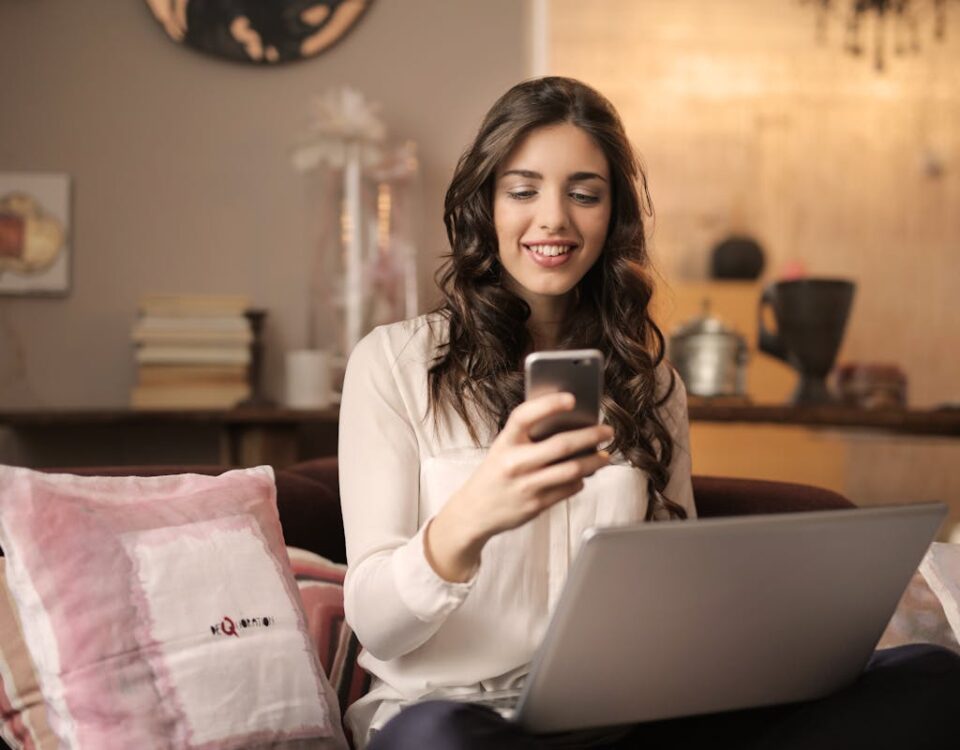 Como economizar na escolha do seu plano de internet Woman Sitting on Sofa While Looking at Phone With Laptop on Lap