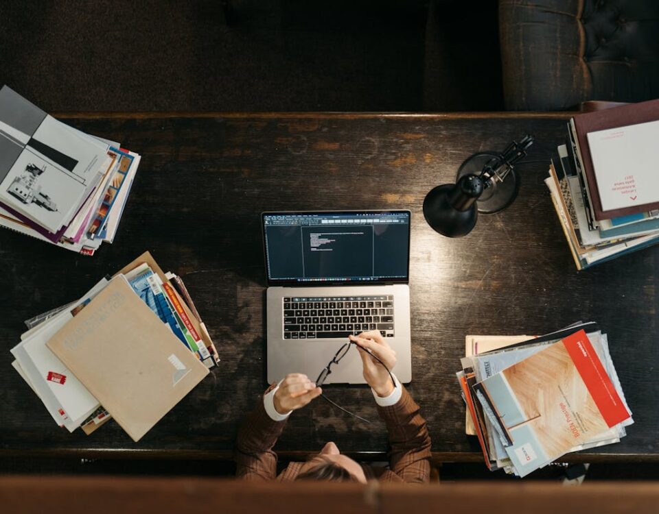 Cursos livres que podem impulsionar sua carreira financeira A Student Sitting behind a Wooden Desk with Stacks of Books and a Laptop