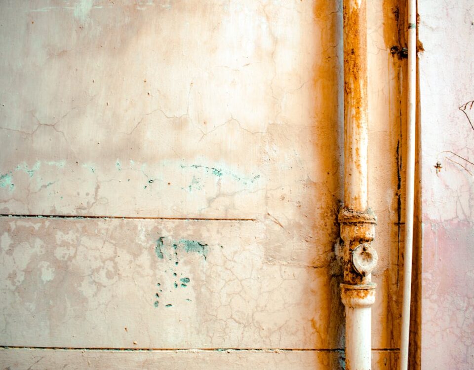 Quanto custa prevenir problemas hidráulicos em casa? Close-up of a rusty pipe on a cracked, weathered wall in rustic tones.