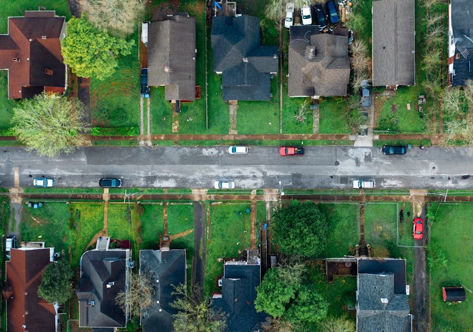 Investimento em loteamento ou apartamento: qual é mais rentável? High-angle aerial shot of a suburban neighborhood street lined with houses and cars.