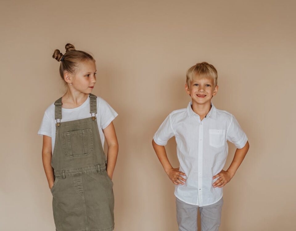 Como economizar ao comprar roupas infantis A smiling brother and sister in casual clothing pose against a neutral background.