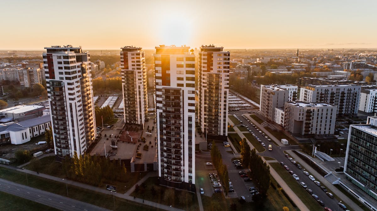 Investimento em loteamento ou apartamento: qual é mais rentável? Captivating high-rise buildings silhouetted by a setting sun in a bustling cityscape.