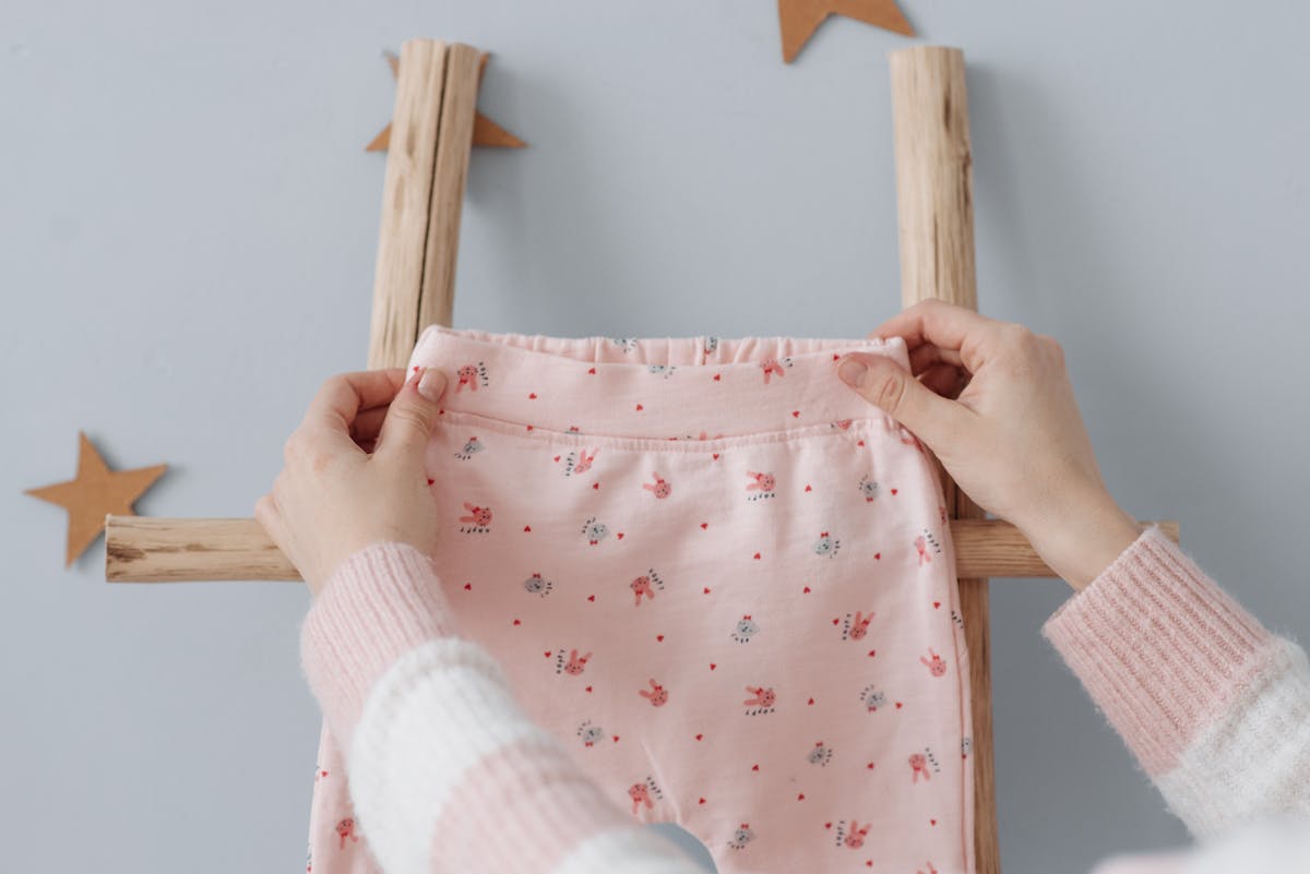 Como economizar ao comprar roupas infantis Soft pink baby trousers held on a ladder with star decorations, indoors.