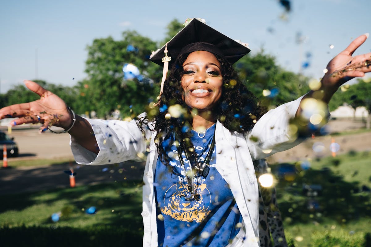 Vale a pena investir em cursos profissionalizantes? African American woman celebrating graduation with confetti outdoors, filled with happiness and success.