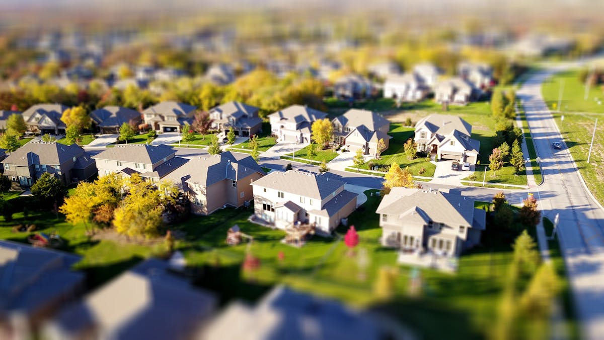 Como calcular o retorno financeiro de uma propriedade Tilt-shift aerial photo of a suburban neighborhood with green lawns and roads.