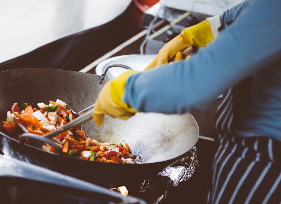 Economizar na cozinha sem abrir mão do sabor A chef stir-frying vegetables in a wok, showcasing vibrant fresh ingredients.