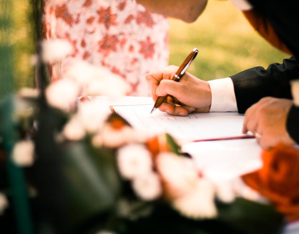 A close-up of hands signing a marriage contract during an outdoor wedding ceremony