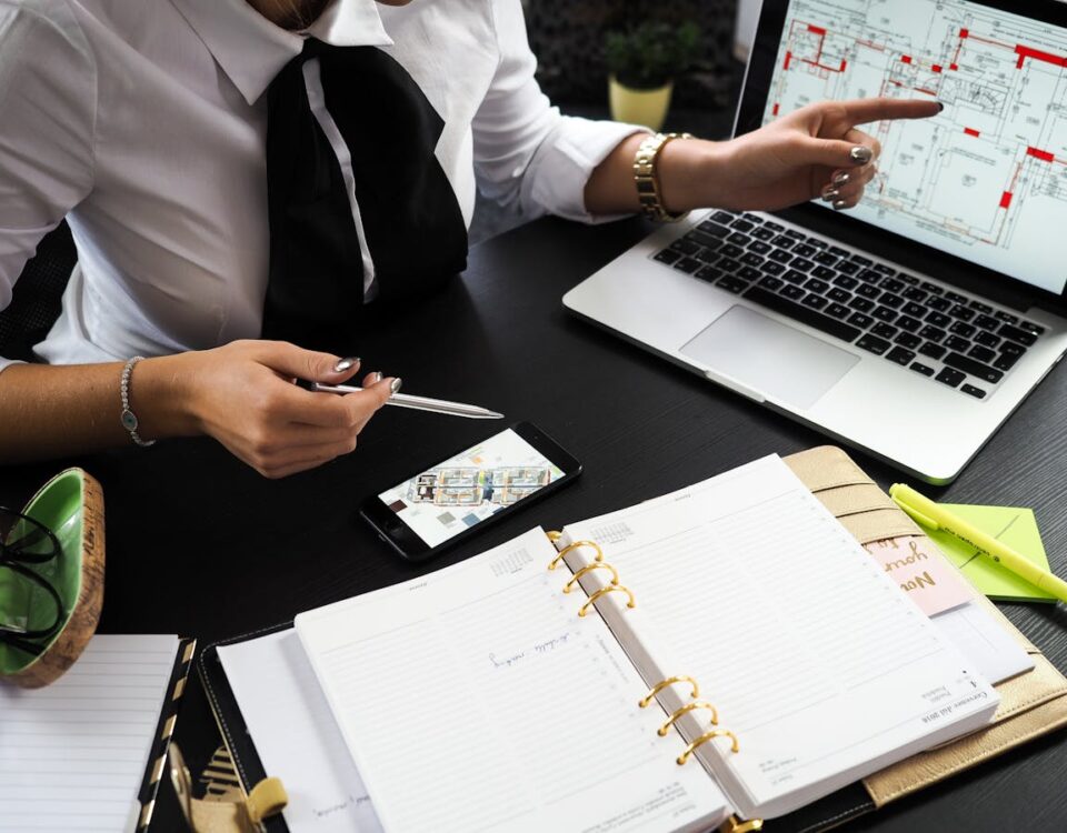 Vale a pena investir em imóveis em tempos de incerteza? A business professional working on real estate project plans using multiple devices in an office setting.