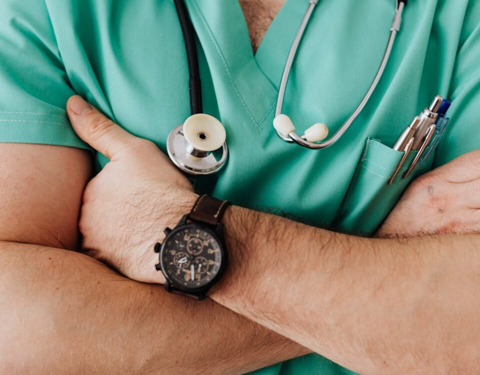 Planos de saúde valem a pena para quem tem DII? Close-up of a healthcare professional with arms crossed wearing medical scrubs and stethoscope.