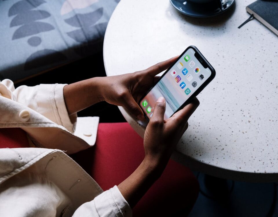 Painéis SMM: Vale a pena investir? A person checks social media apps on a smartphone while sitting at a café table.