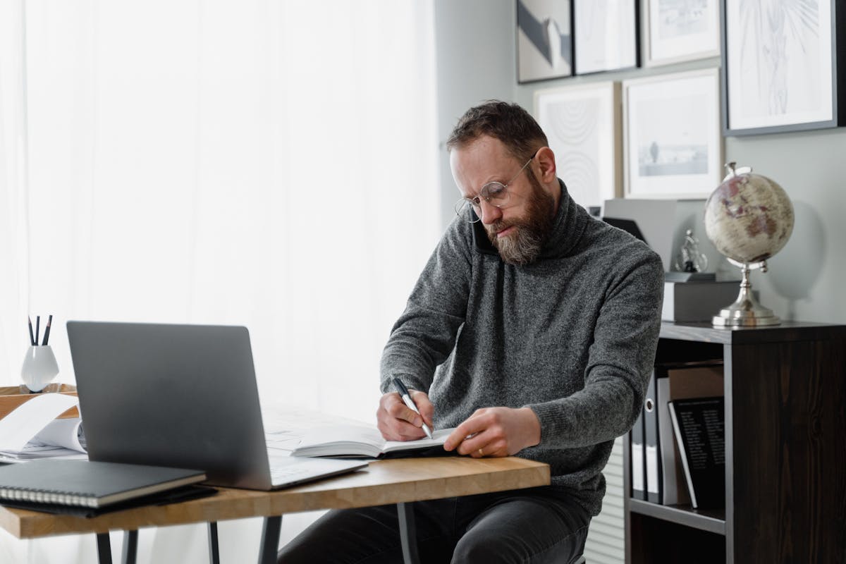 Quanto custa tirar a CNH? Man concentrating on work at home office desk with laptop and documents.