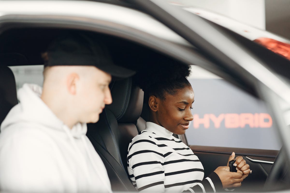 A man and woman sitting inside a hybrid car, discussing its features, highlighting modern eco-friendly transportation.