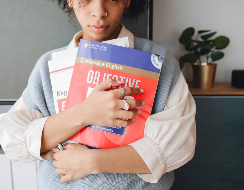 Vale a pena investir em cursos de idiomas? Young woman holding language study books indoors, symbolizing education and learning.