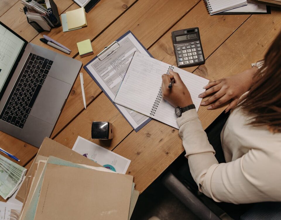 Salário e benefícios do auxiliar administrativo em 2025 Focused woman calculating figures at office desk with a laptop and documents.