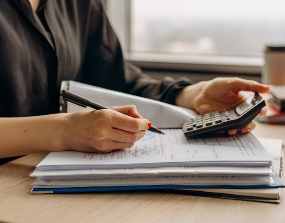 O segredo por trás da redução de custos em grandes indústrias Close-up of person using a calculator with financial documents in an office.