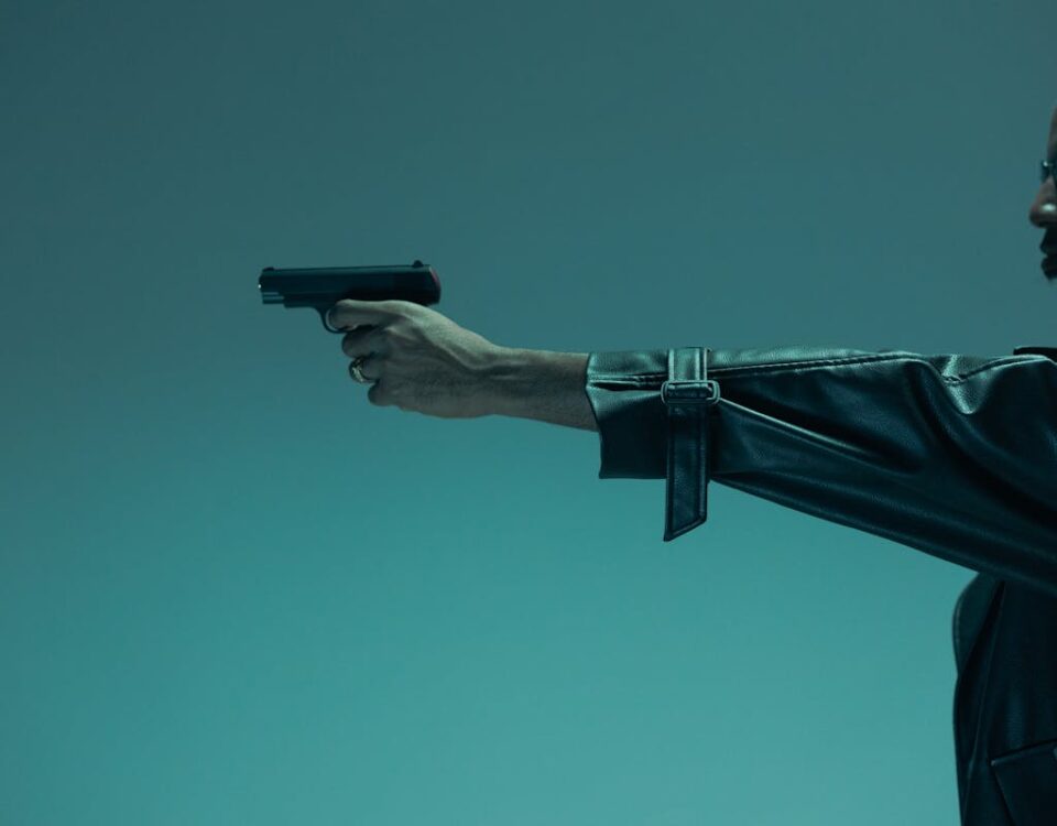 O impacto econômico de possuir armas legalizadas Side view of a man in a leather jacket holding a handgun, conveying a theme of defence and danger.