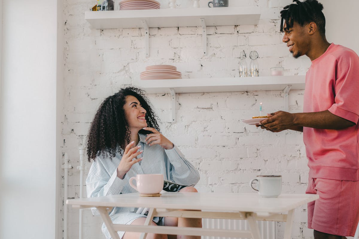 Como economizar na compra de itens para decoração da casa Happy couple celebrating a birthday with breakfast indoors, featuring a lit candle on a plate.