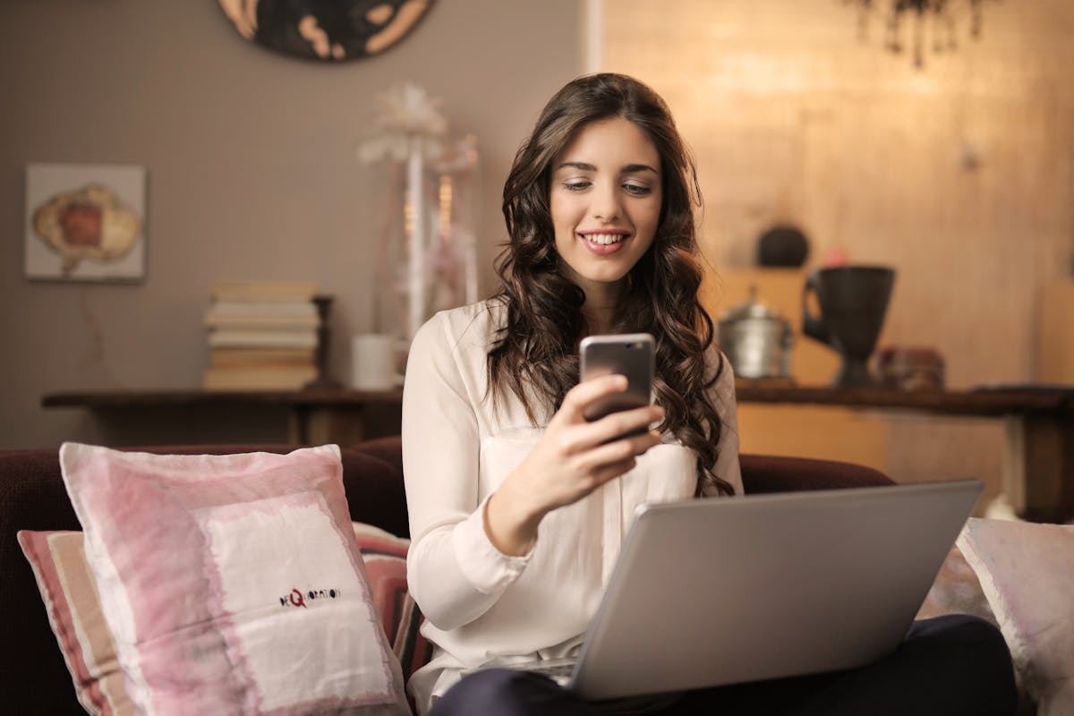 Painéis SMM: Vale a pena investir? A woman enjoying leisure time using her smartphone and laptop in a cozy living room.