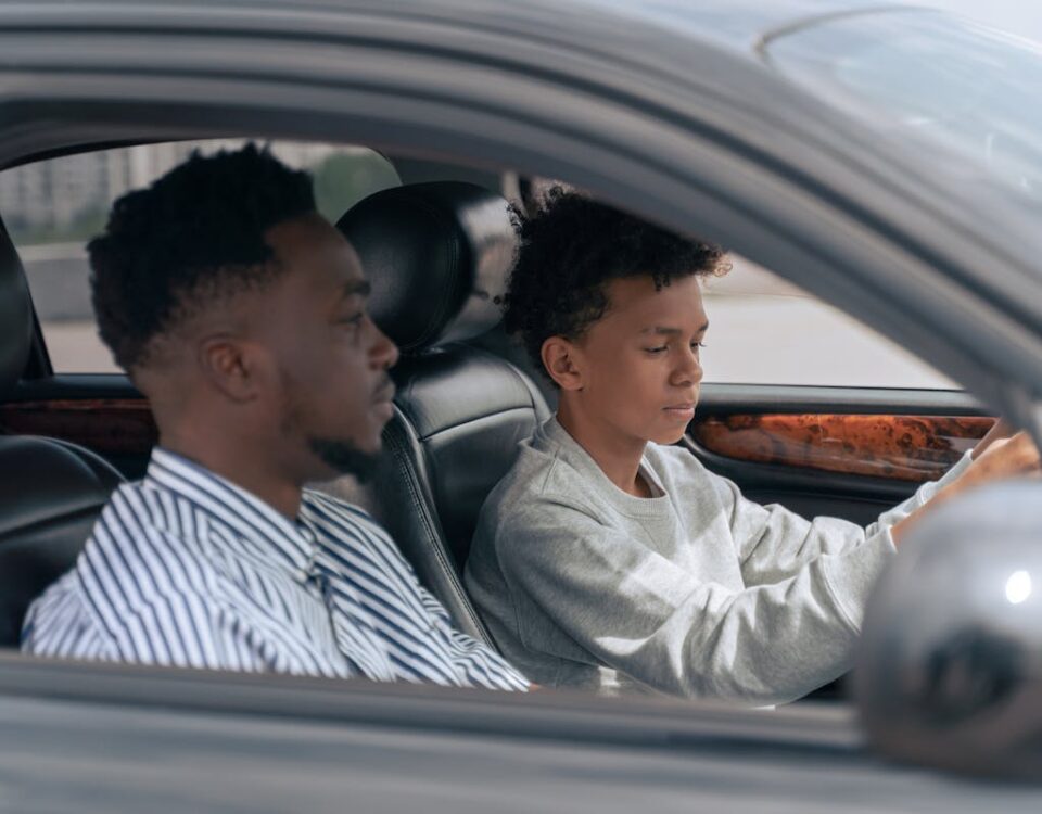 Vale a pena parcelar a autoescola? A father sits beside his son who is learning to drive, inside a car.
