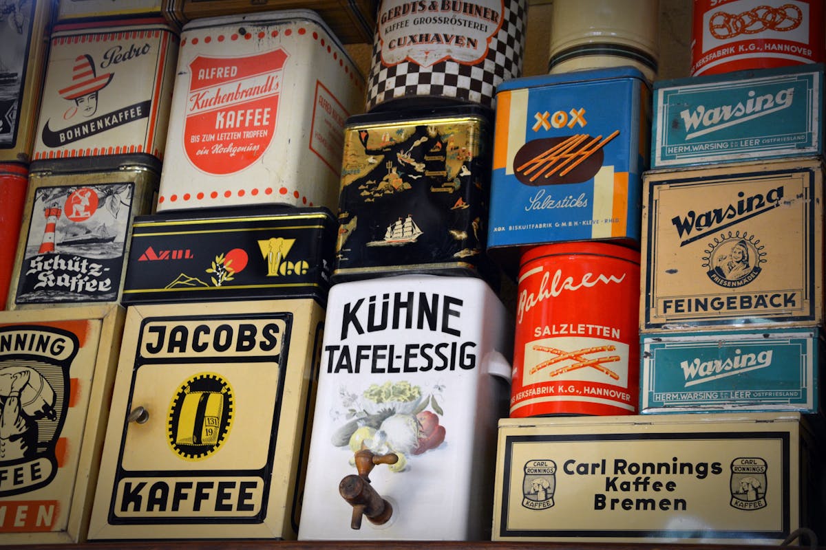 Como calcular o custo-benefício na compra de rótulos adesivos Diverse vintage German coffee tins and other containers displayed on a shelf showcasing nostalgic packaging.