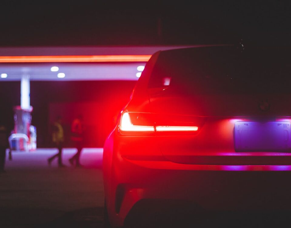 Como calcular os custos diários de dirigir um carro A night shot of a car's tail lights glowing under gas station lights.