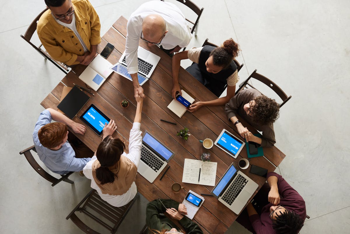 Como empresas de TI economizam com tecnologia? Top view of a diverse team collaborating in an office setting with laptops and tablets, promoting cooperation.