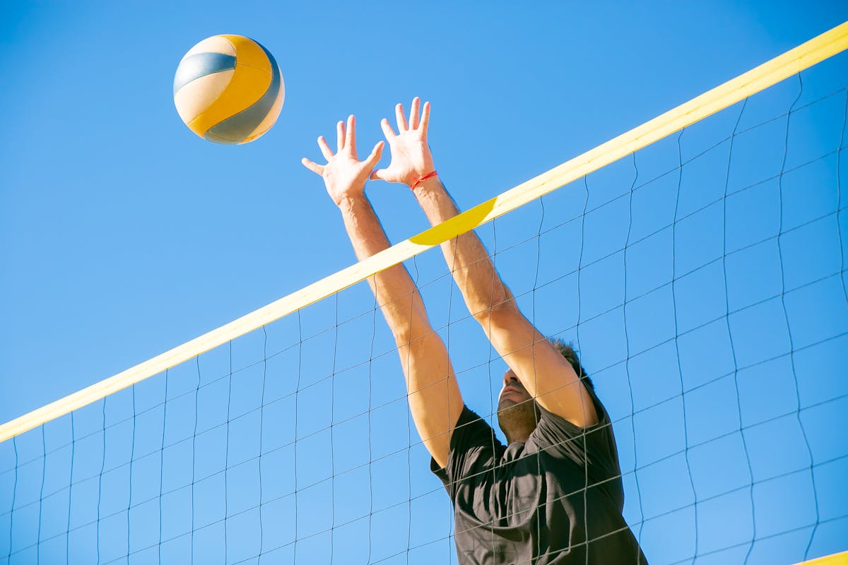 Como aumentar a rentabilidade da sua arena esportiva Dynamic outdoor volleyball game with a male player blocking a ball under clear blue skies.