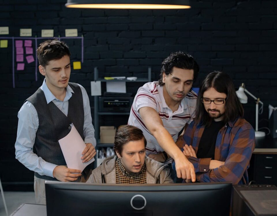 Como empresas de TI economizam com tecnologia? Group of professionals discussing a project at a computer in a modern office environment.