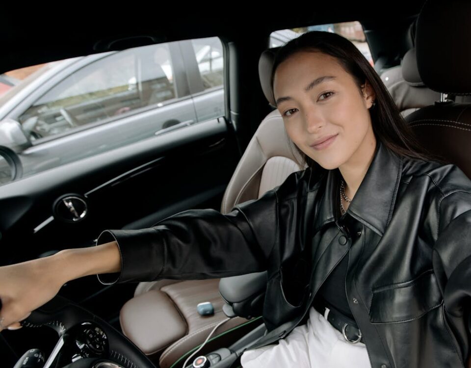 Quanto custa tirar a CNH em 2025? A young woman in a black leather jacket takes a selfie inside a modern car, showcasing a relaxed pose.