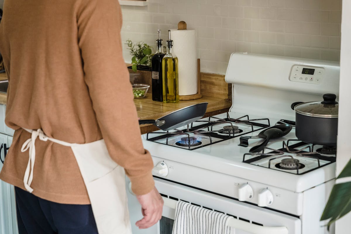Cozinhar em casa: Quanto você economiza realmente? A person preparing food on a gas stove in a cozy kitchen setting.