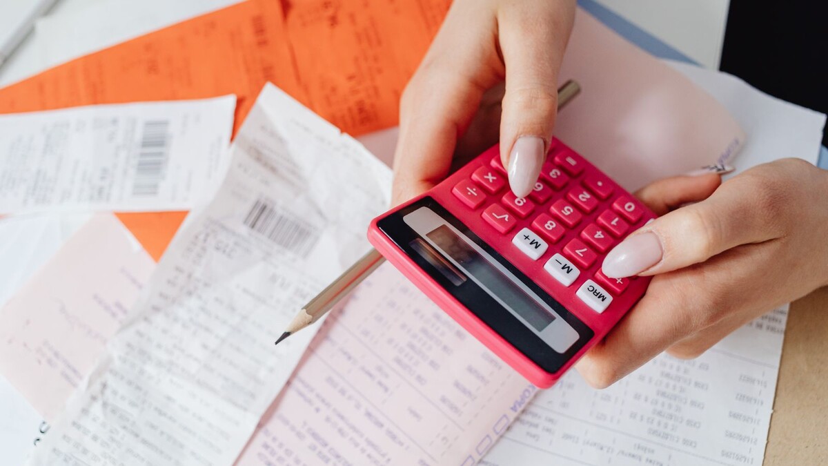 Mãos usando uma calculadora rosa sobre recibos e papéis