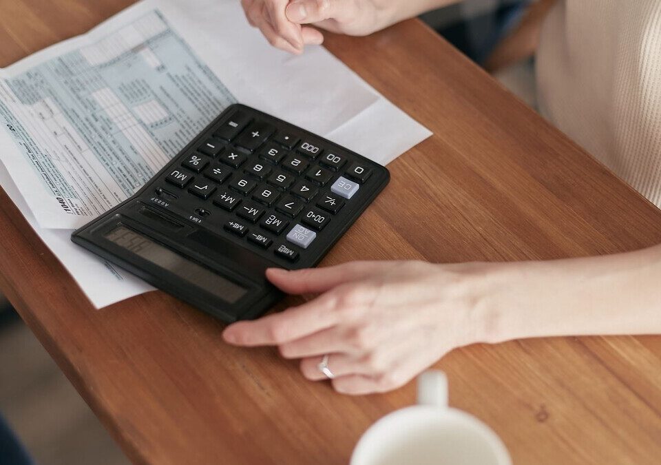 Pessoa fazendo contas com calculadora e papéis sobre uma mesa de madeira
