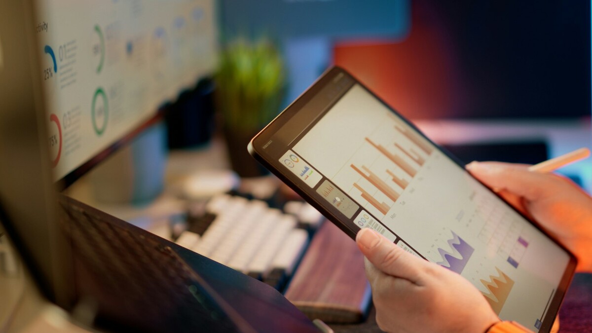 Mãos segurando um tablet com gráficos de barras e dados financeiros