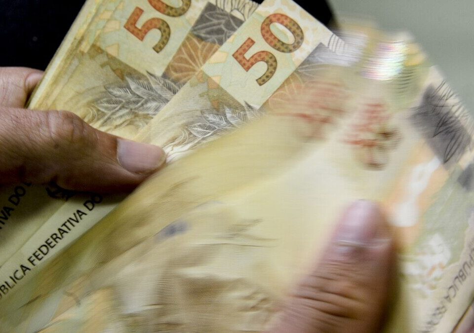 Mãos contando cédulas de 50 reais