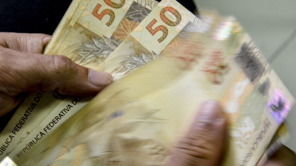 Mãos contando cédulas de 50 reais