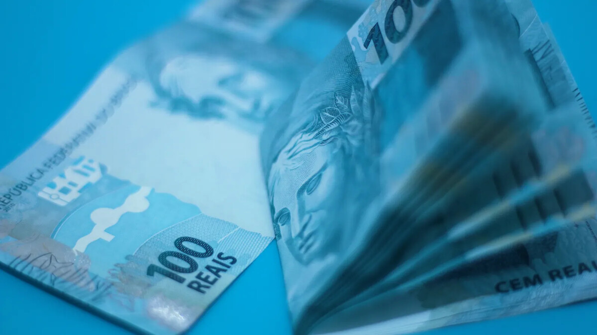 Pilha de cédulas de 100 reais sobre superfície azul