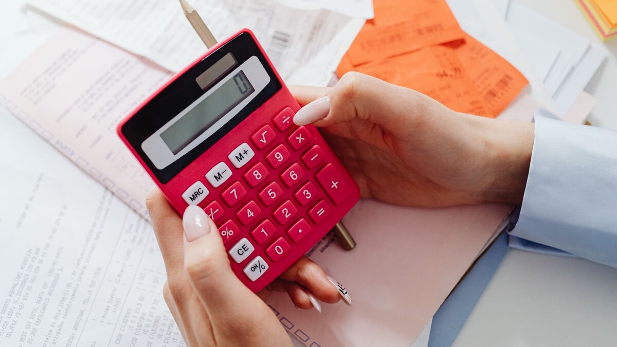Mãos segurando uma calculadora vermelha sobre papéis e recibos