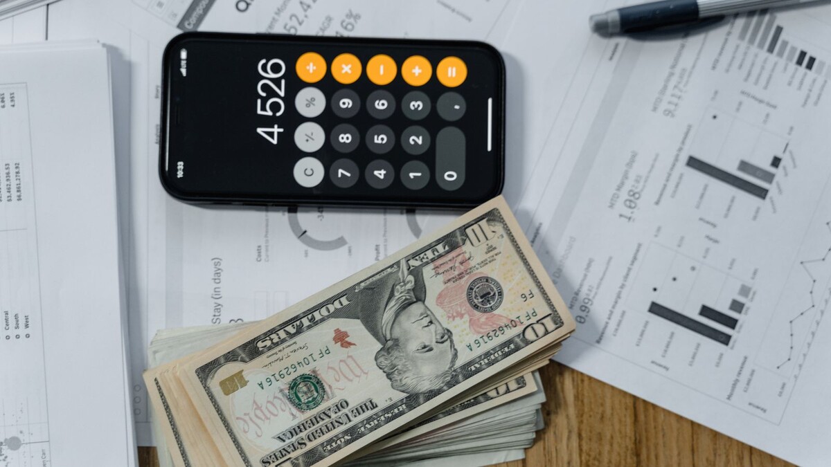 Celular com calculadora aberta ao lado de cédulas e documentos sobre uma mesa