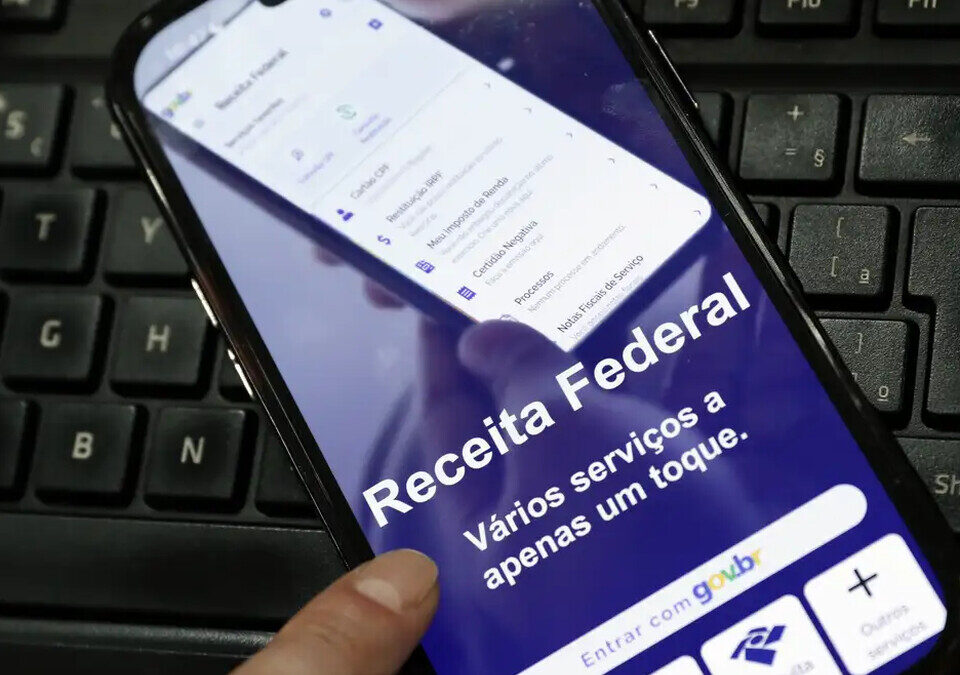 Celular com o aplicativo da Receita Federal aberto sobre um teclado de computador