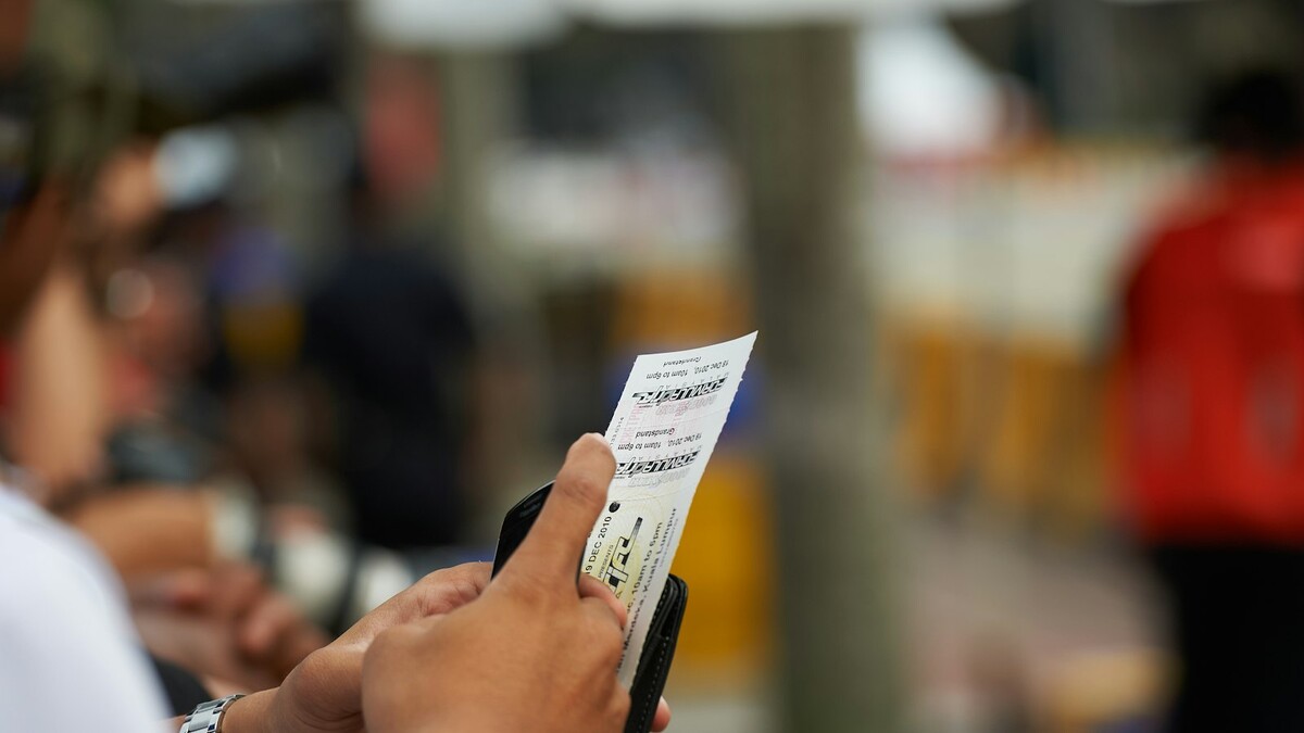 Mão segurando um bilhete de loteria impresso com fundo desfocado