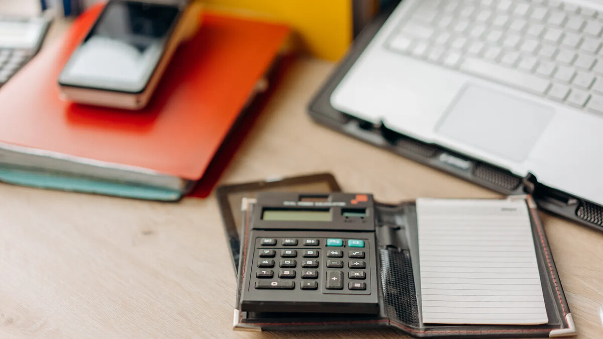 R$ 200 bilhões para pagar dívidas: o que foi prometido? Calculadora e caderno ao lado de um computador sobre uma mesa