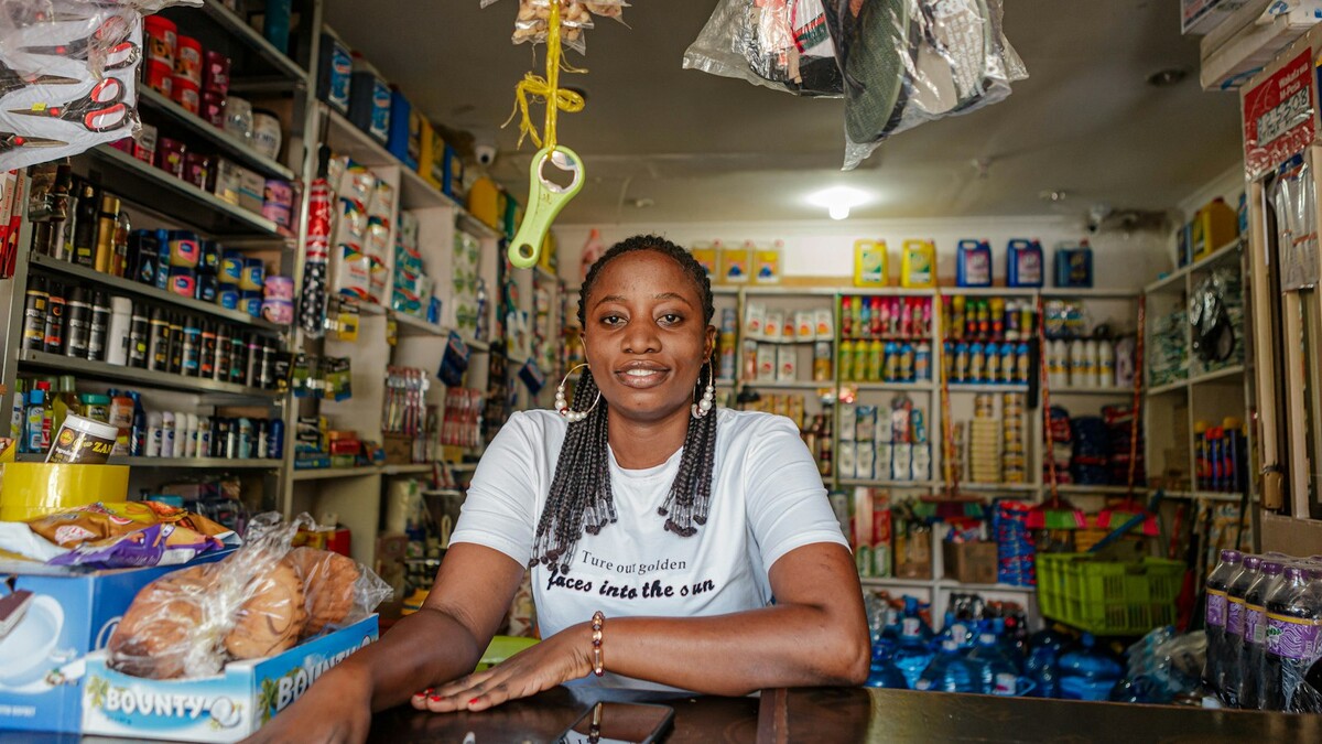 Comerciante sorridente atrás do balcão de uma pequena loja com prateleiras cheias